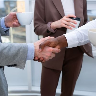 A professional handshake between colleagues holding coffee cups, symbolizing collaboration.
